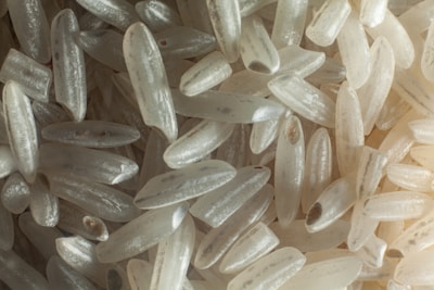 Close-up view of numerous grains of white rice with a variety of sizes and slight translucence, highlighting the texture and structure of each grain.