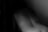 A black and white photograph featuring a person's back with a focus on the curve of the spine. The lighting is dim, creating a shadowy, mysterious effect.