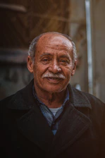 A candid portrait of John Sele Philip smiling warmly against a softly blurred urban background.