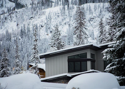 Modern townhouse nestled among tall pine trees with mountain peaks in the background.