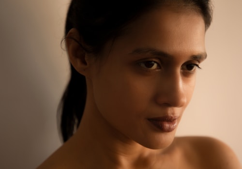 A close-up portrait of a person with a neutral expression, featuring soft lighting that creates subtle shadows on the face and a blurred background.
