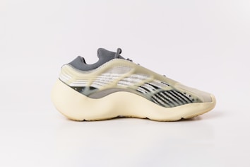 A modern sneaker with a sleek, futuristic design featuring a translucent upper and contoured sole. The shoe combines various textures and patterns, incorporating shades of beige, gray, and black for a sophisticated look.