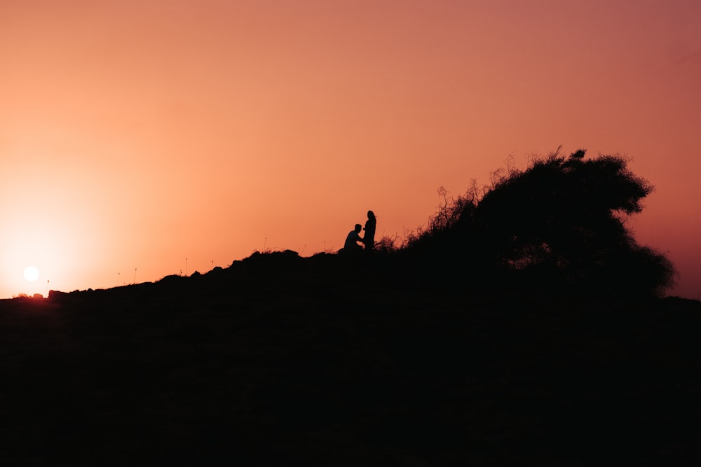 a silhouette of a person and a person on a hill at sunset