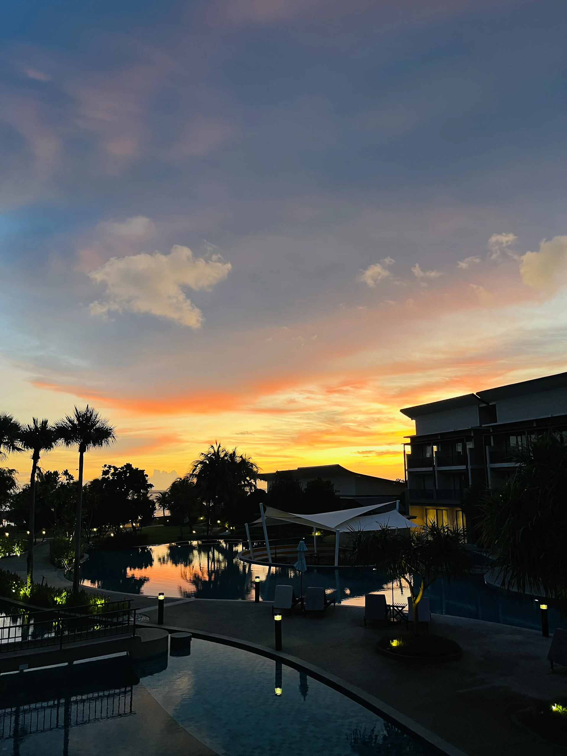 A serene sunset casting golden hues over a modern resort pool surrounded by palm trees.