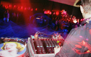 A lively DJ mixing tracks at Los 300 de Gedeón studio with colorful lights