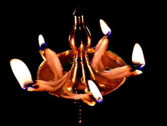 A beautifully lit traditional kuthu vilakku lamp made of polished brass, glowing warmly against a white and gold backdrop.