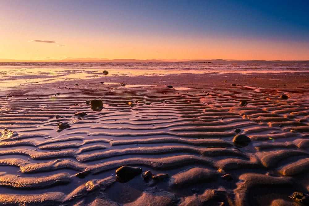 a body of water with rocks and a sunset in the background