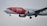 A commercial airplane in flight with a red and white paint scheme, featuring branding for RIU Hotels & Resorts, and websites TUI.COM. The airplane is captured in mid-air with its landing gear extended against a cloudy sky.