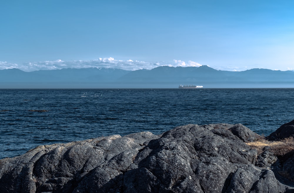 a rocky shore with a body of water and a large ship in the distance