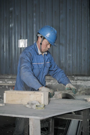 Team of workers wearing blue uniforms collaborating around a large metal fabrication table
