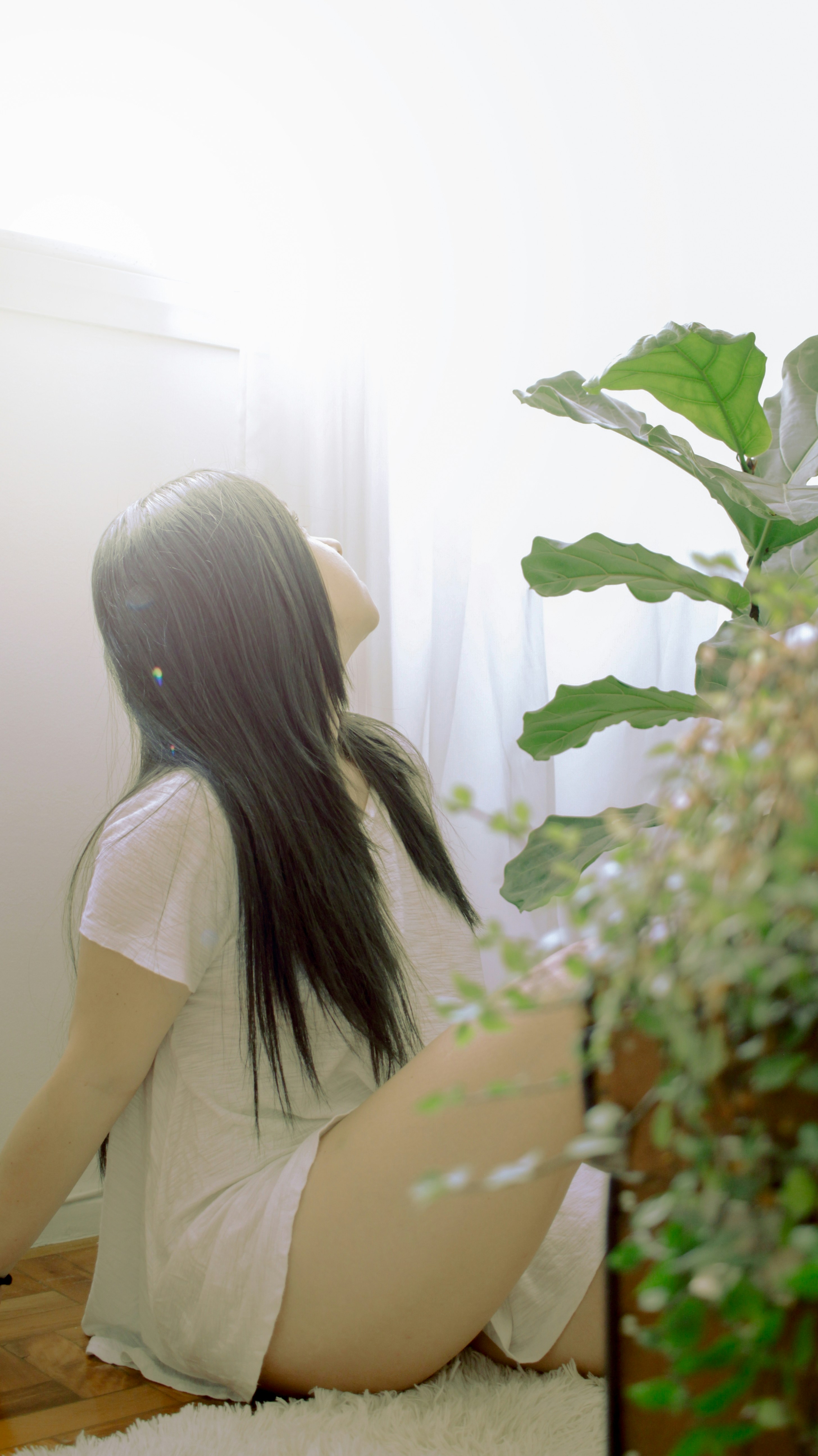 Woman sitting on floor near potted plant.