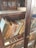 An antique wooden bookcase with glass doors holds a collection of old, worn books with varying cover colors and visible signs of aging. Some books have faded or torn spines, and dust is present on the shelves, indicating infrequent use.