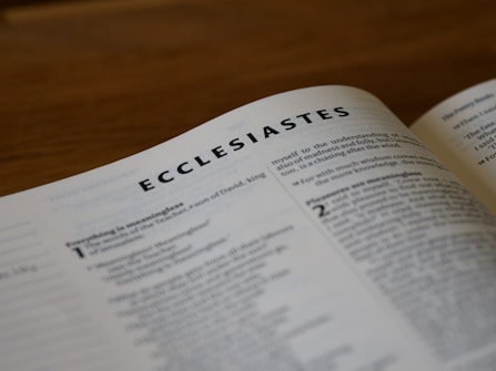 A close-up view of an open page from a book, specifically showing the beginning of the book of Ecclesiastes with the title in bold. The text appears to be well lit, with smaller text visible but not completely legible in the foreground and background.