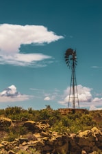 A rustic windmill standing tall over green pastures at sunrise on the mini farm.