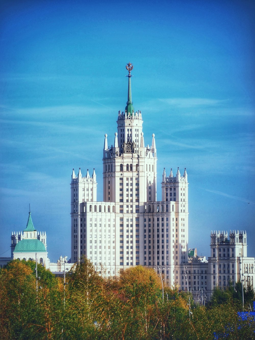 a large white building with a green dome and trees in front of it