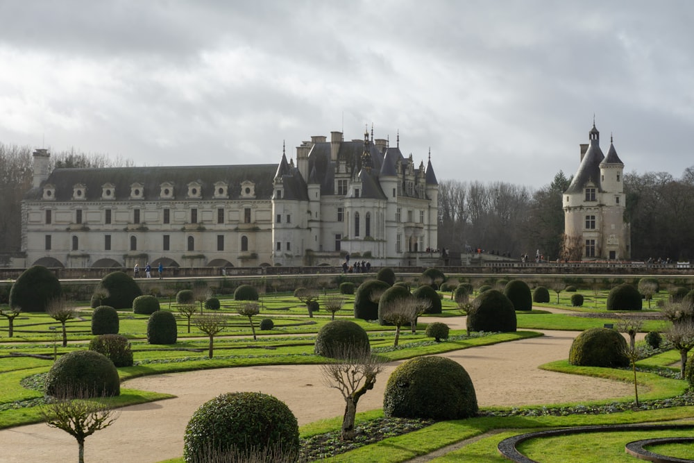 un grand bâtiment avec de nombreux buissons devant lui avec le château de Chenonceau en arrière-plan