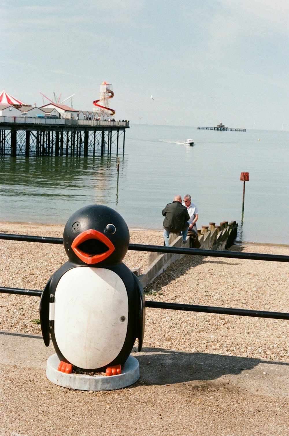 a penguin statue on a sidewalk by a body of water