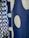 A close-up view of a blue fabric featuring large white polka dots in a vertical pattern. The fabric texture is visible, lending a tactile quality to the image. The polka dots vary slightly in size and are evenly spaced across the fabric.
