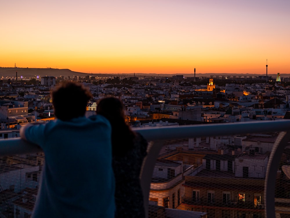 a man and woman kissing on a balcony overlooking a city