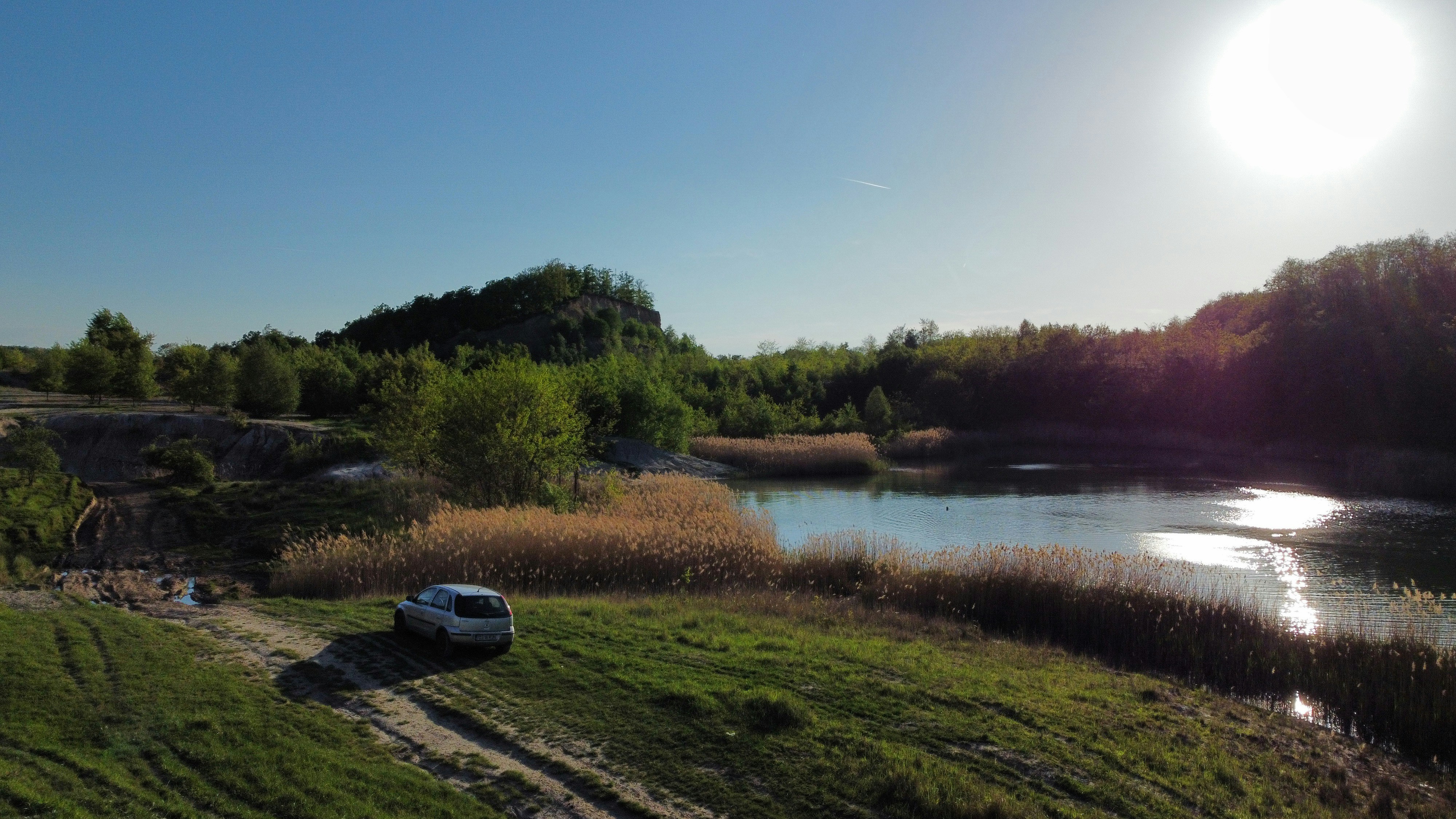 a car on a road by a river with trees and grass