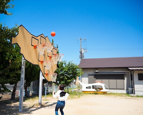A person kicking a soccer ball towards colorful vertical hoops on a sunny day.