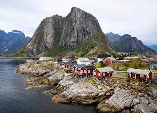 a group of houses by a body of water with mountains in the background with Lofoten in the background