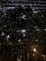 Black and white shot of rain droplets on a window, blurring the city lights beyond.