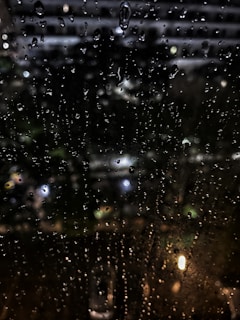Black and white shot of rain droplets on a window, blurring the city lights beyond.