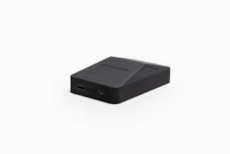 A small, black, rectangular electronic device with a sleek design. It includes a USB port, a micro USB port, and multiple small indicator lights on one side. The surface has geometric lines and a partially elevated section.