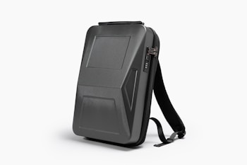 A sleek, black, hard-shell backpack with an ergonomic design. The front panel features distinct geometric patterns and a combination lock. The backpack has adjustable shoulder straps and a streamlined appearance, suitable for modern, urban settings.