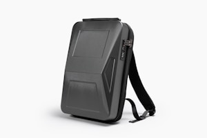 A sleek, black, hard-shell backpack with an ergonomic design. The front panel features distinct geometric patterns and a combination lock. The backpack has adjustable shoulder straps and a streamlined appearance, suitable for modern, urban settings.