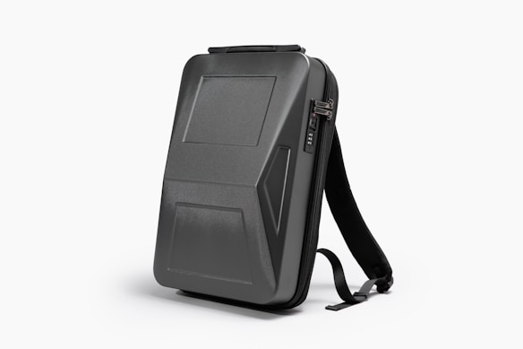 A sleek, black, hard-shell backpack with an ergonomic design. The front panel features distinct geometric patterns and a combination lock. The backpack has adjustable shoulder straps and a streamlined appearance, suitable for modern, urban settings.