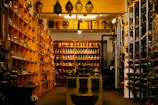 A shop interior filled with various cultural and decorative items, including masks, statues, and bowls displayed on shelves and tables. The shelves are organized with items displayed in an orderly fashion, and there is dim lighting creating a cozy atmosphere.