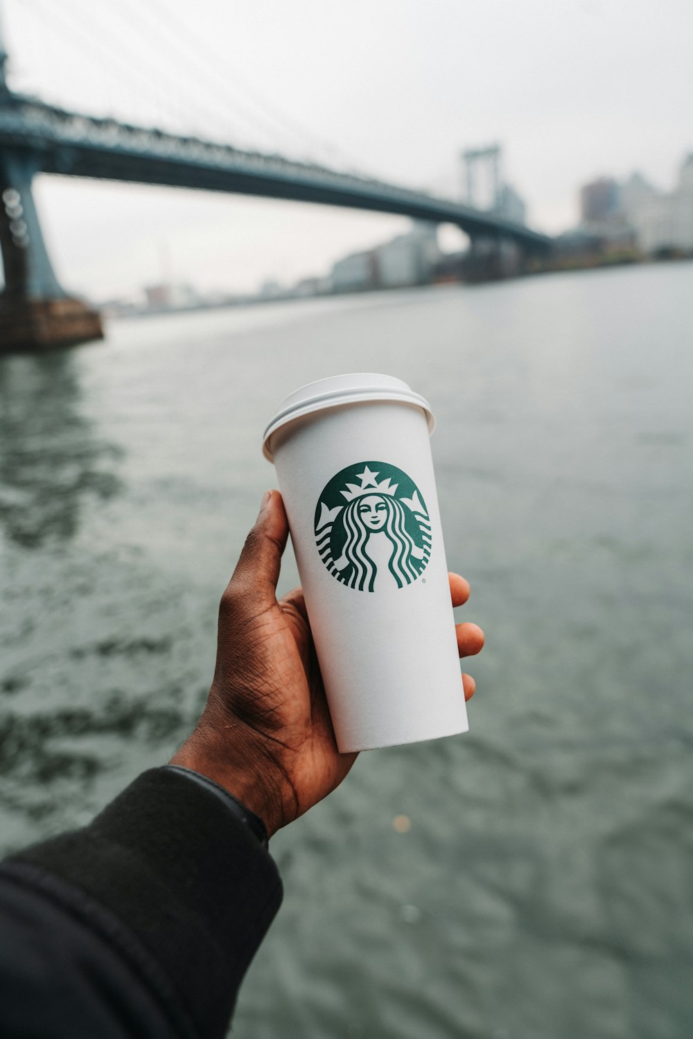 a hand holding a white cup with a green logo on it