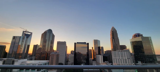 A modern city skyline at sunset with warm golden light reflecting off glass buildings.
