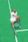A person wearing a white sports outfit is sitting on a bright green tennis court. The individual has their eyes closed and appears relaxed. They are holding a tennis racket in one hand, and wearing gray sneakers and blue patterned socks.