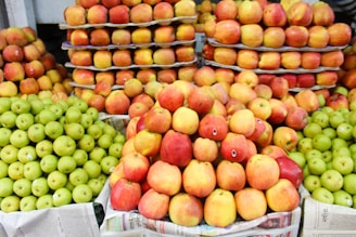 A vibrant display of apples, with piles of red and green apples neatly arranged on tiers made from cardboard and newspaper. The apples are fresh and shiny, suggesting they are ripe and ready to be purchased.