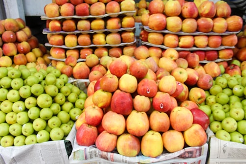 A vibrant display of apples, with piles of red and green apples neatly arranged on tiers made from cardboard and newspaper. The apples are fresh and shiny, suggesting they are ripe and ready to be purchased.