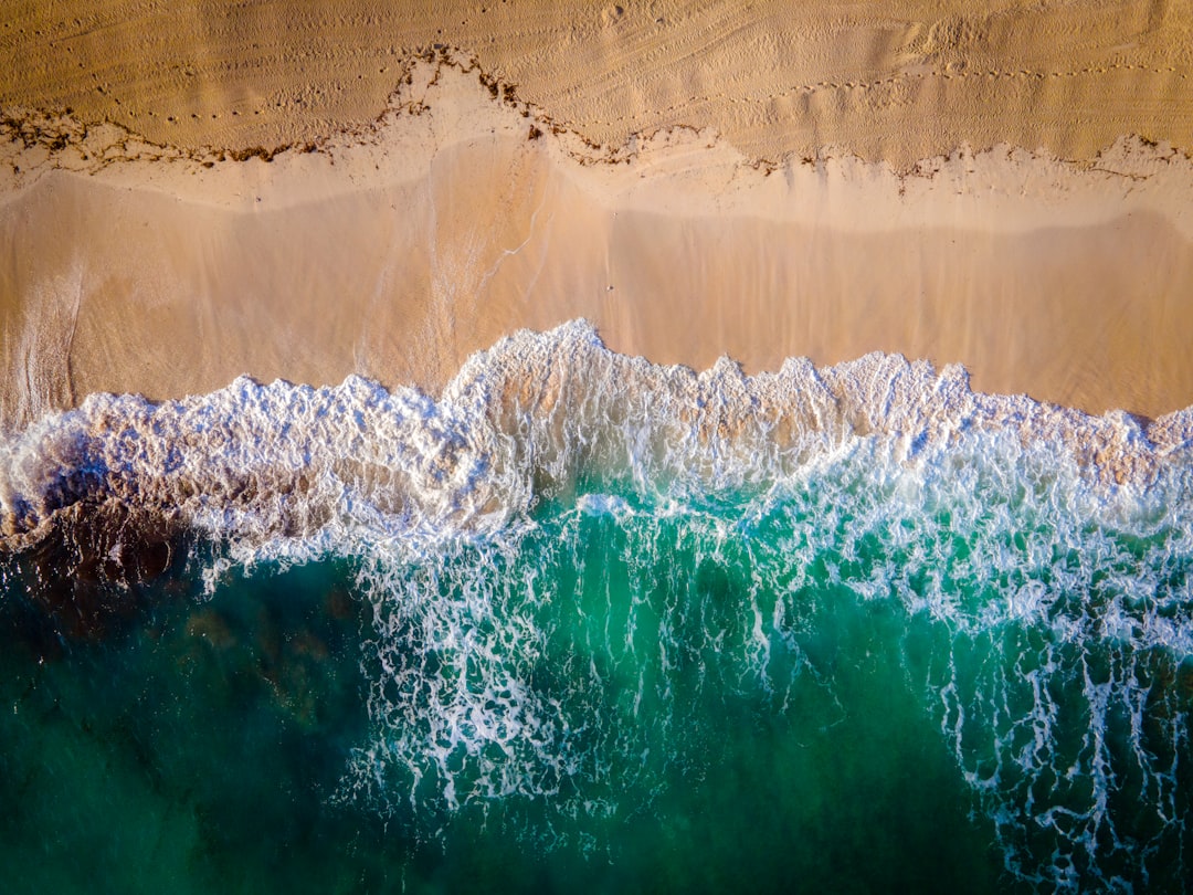 a wave crashing against a wall, drone picture of a wave breaking on a beach