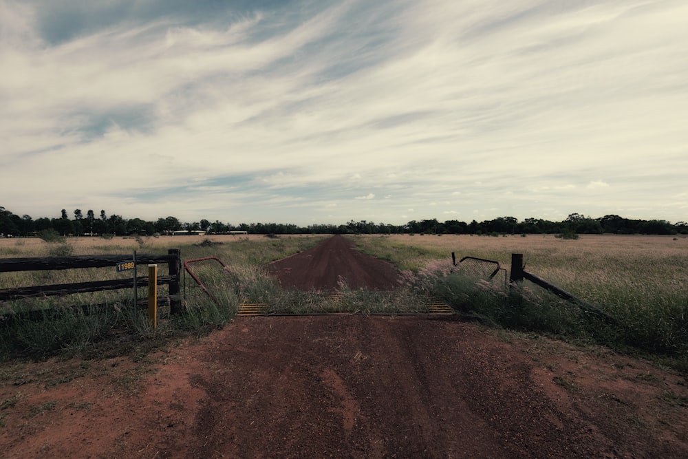 a dirt road with a fence and grass on the side