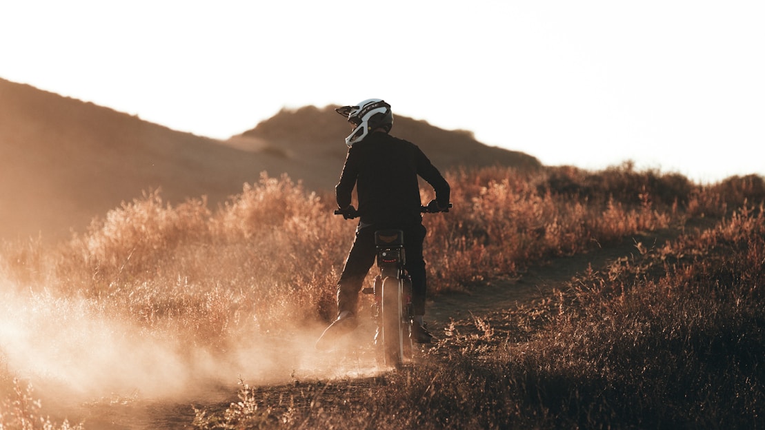 A rugged dirt bike kicking up dust on a forest trail at sunset.
