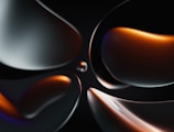Smooth, abstract shapes with glossy surfaces in a dark setting, featuring reflections and highlights. A combination of metallic and warm tones gives the image a sleek, futuristic feel.