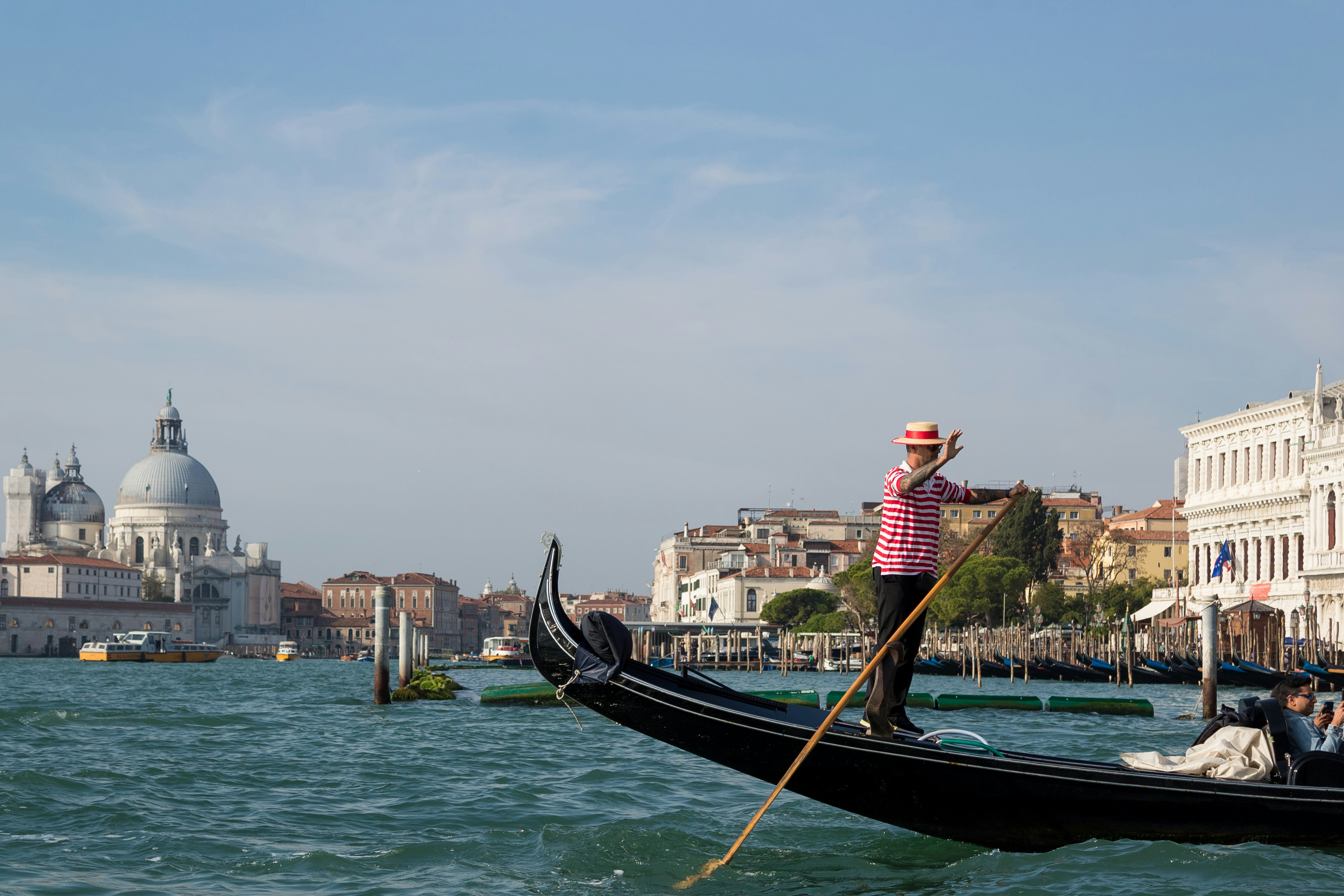a person in a boat with a dragon head, Waving at the tourists in the Vaporetto from the Gondola.