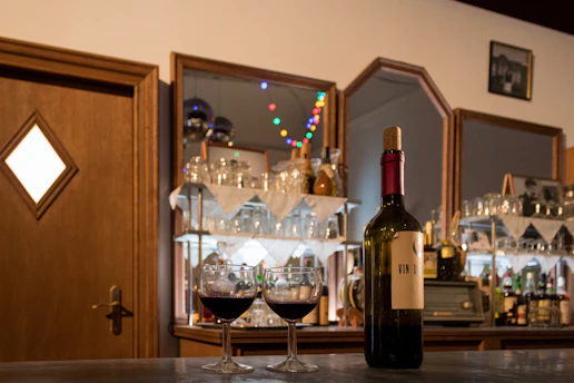 Cozy wine bar corner with glasses and a bottle on a wooden table, soft warm lighting creating an inviting atmosphere.