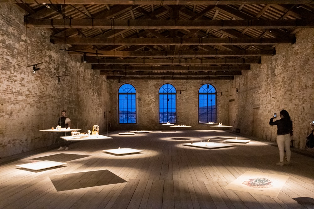 a person taking a picture of a person sitting at a table in a large room with windows