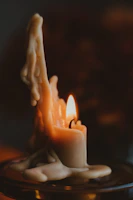 A partially melted candle with wax drippings flowing down its sides, casting a warm and gentle glow. The flame flickers softly, illuminating the surrounding wax, which has formed organic, layered patterns as it cools and hardens.