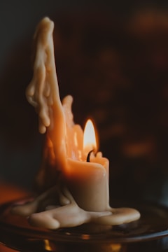 A partially melted candle with wax drippings flowing down its sides, casting a warm and gentle glow. The flame flickers softly, illuminating the surrounding wax, which has formed organic, layered patterns as it cools and hardens.