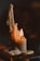 A partially melted candle with wax drippings flowing down its sides, casting a warm and gentle glow. The flame flickers softly, illuminating the surrounding wax, which has formed organic, layered patterns as it cools and hardens.