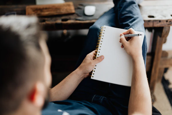 Pessoa escrevendo em um caderno de anotações sobre a mesa de trabalho