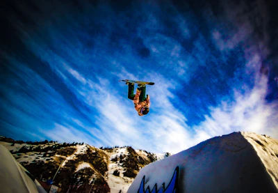 A vibrant photo of a young person snowboarding down a mountain with a clear blue sky.